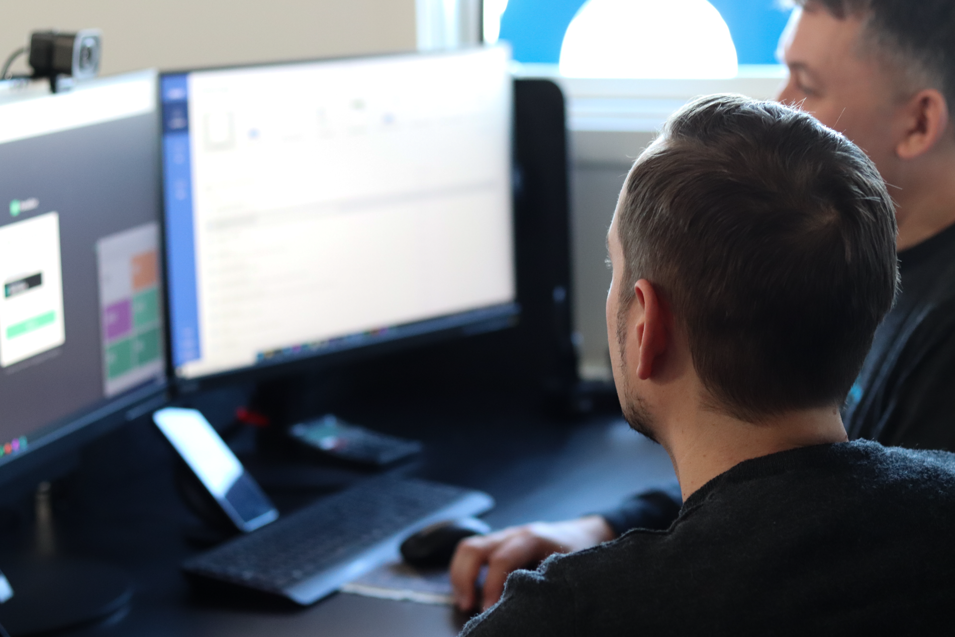 To mænd sidder ved et skrivebord og ser på en computerskærm.