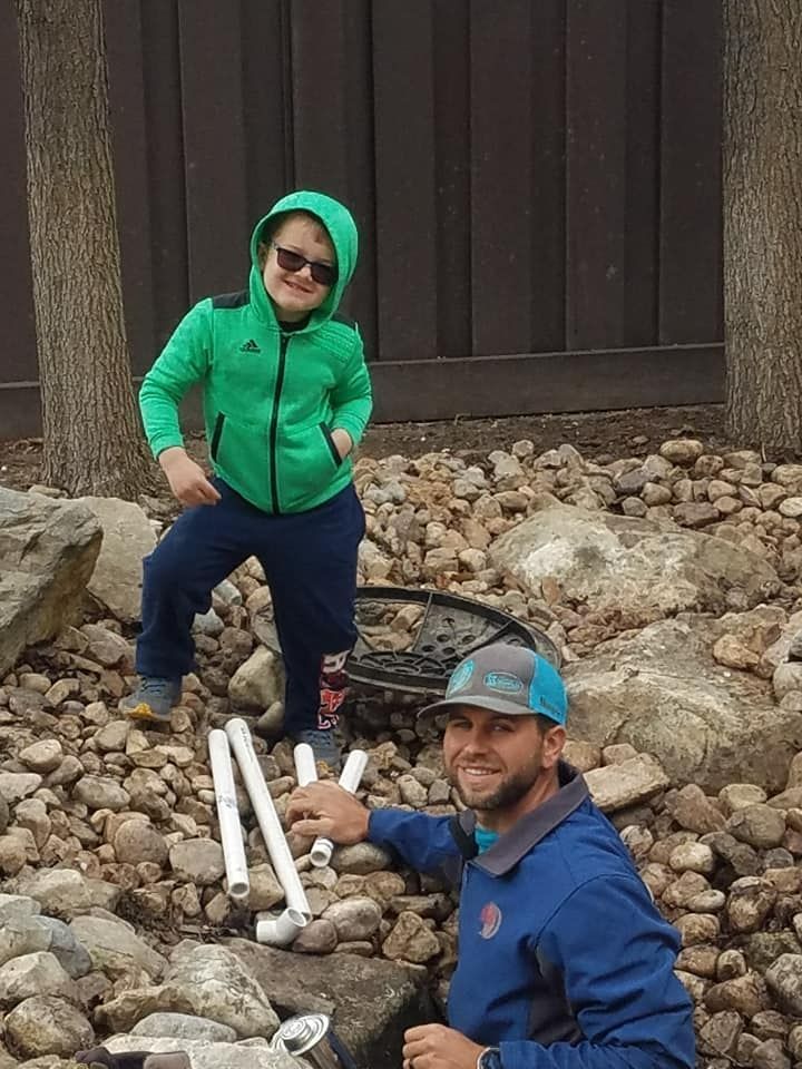 A man and child with PVC pipes among rocks; child smiles, man looks at the camera.