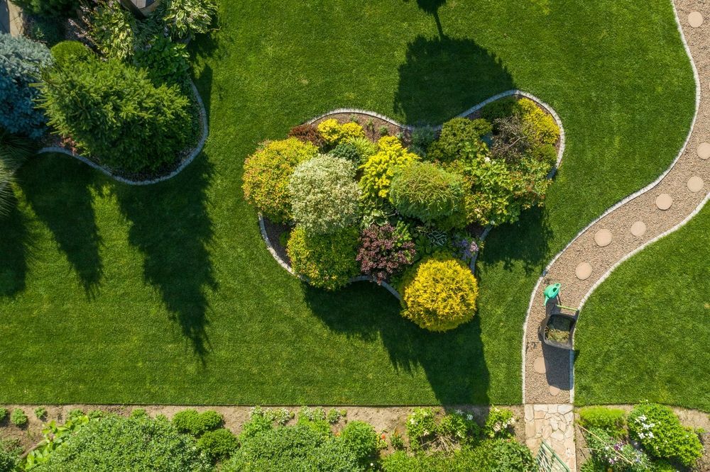 Overhead view of a well-manicured garden with a winding stone path, lush green lawn, and diverse colorful foliage.