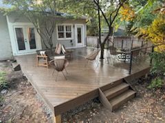 Wooden deck with steps, furnished with chairs, near a house with French doors.