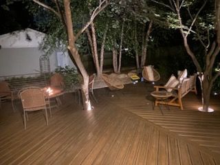 Nighttime backyard deck with outdoor furniture, trees, and ground lighting.