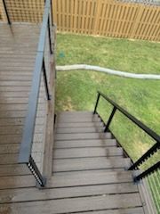 Wooden deck with staircase descending to a grassy yard, black handrails.