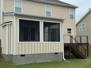 Tan and white screened porch attached to a two-story beige house with a dark brown deck.