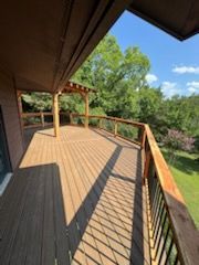 Wooden deck with railing overlooking a grassy yard and trees under a sunny sky.