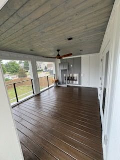 Covered outdoor deck with stained wood floor, gray ceiling, and white trim.
