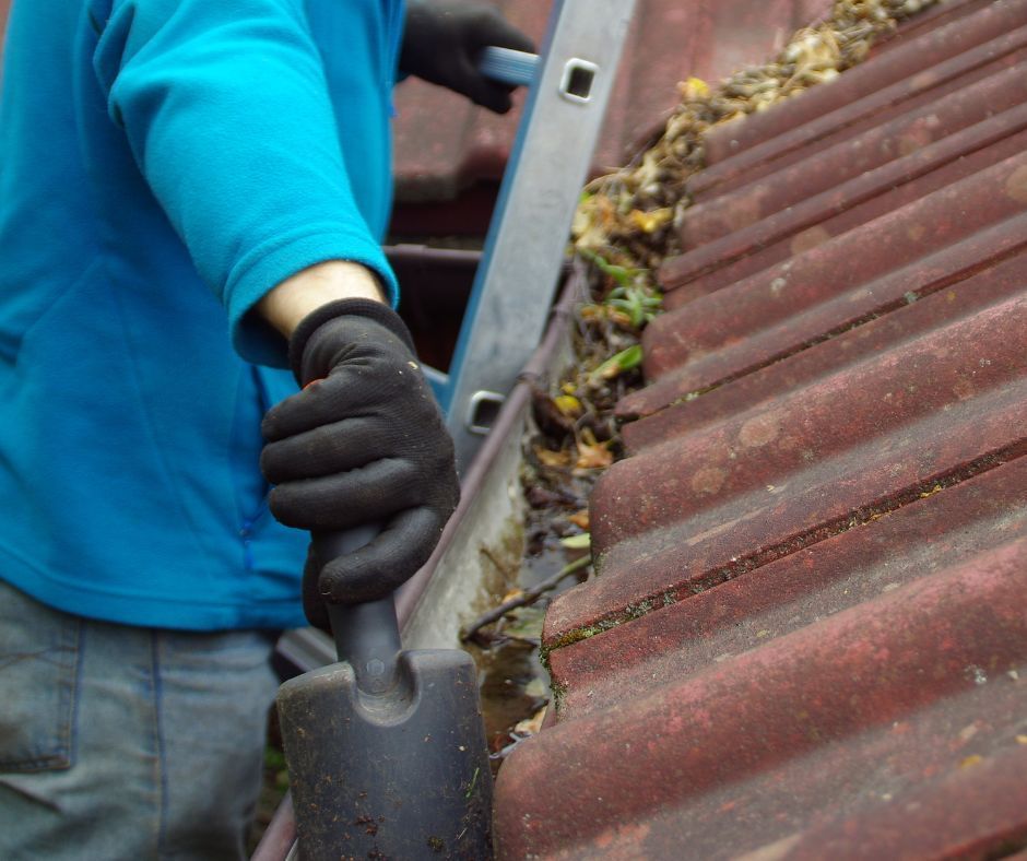 A tradie cleaning debris from a roof gutter.