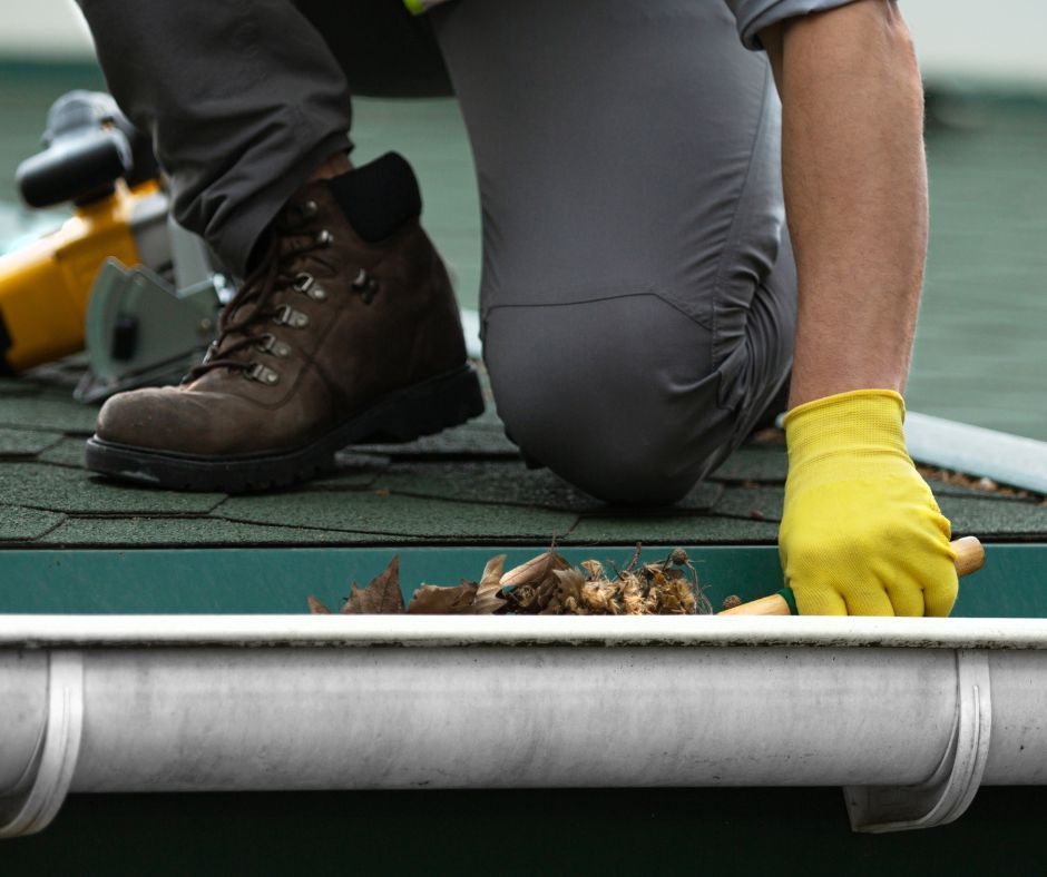 Professional roofer clearing debris from a gutter.