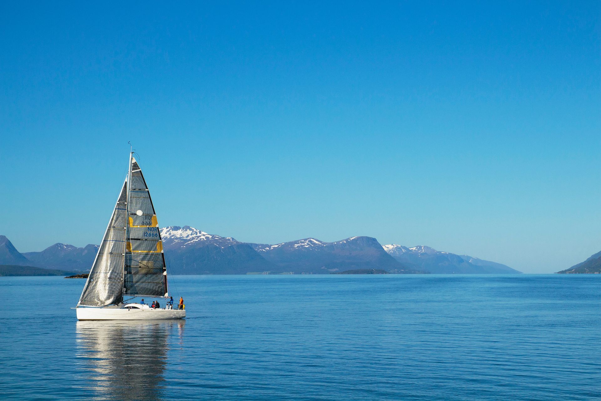 Sailboat on blue water with mountains in the background under a clear sky.