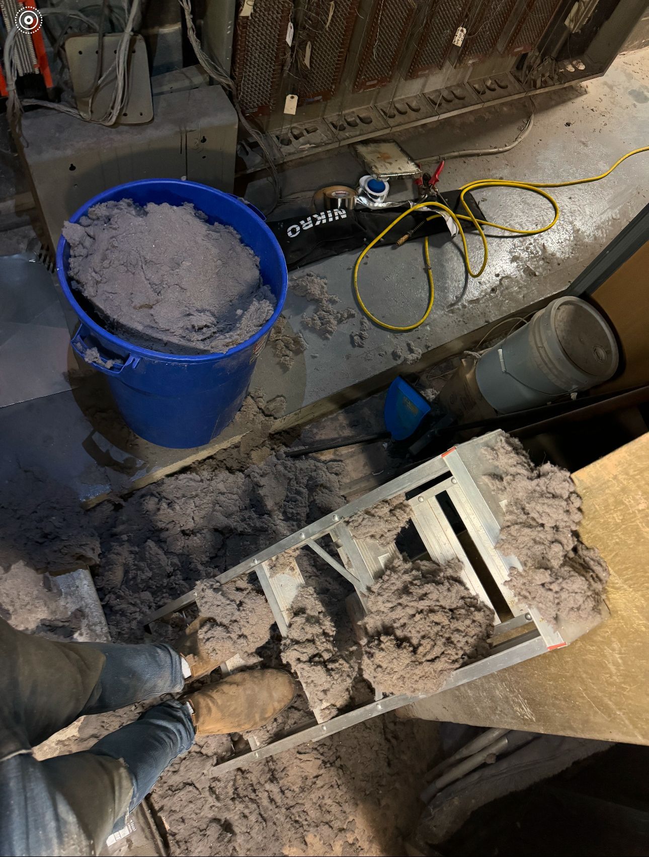 A blue bucket filled with dust is sitting on the floor next to a ladder.