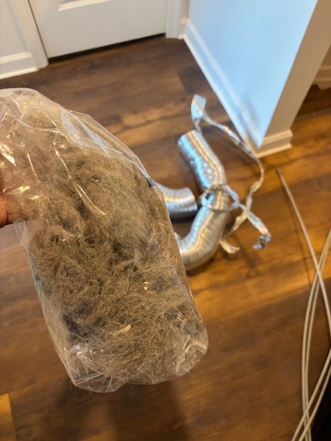 A person is holding a bag of dryer lint on a wooden floor.
