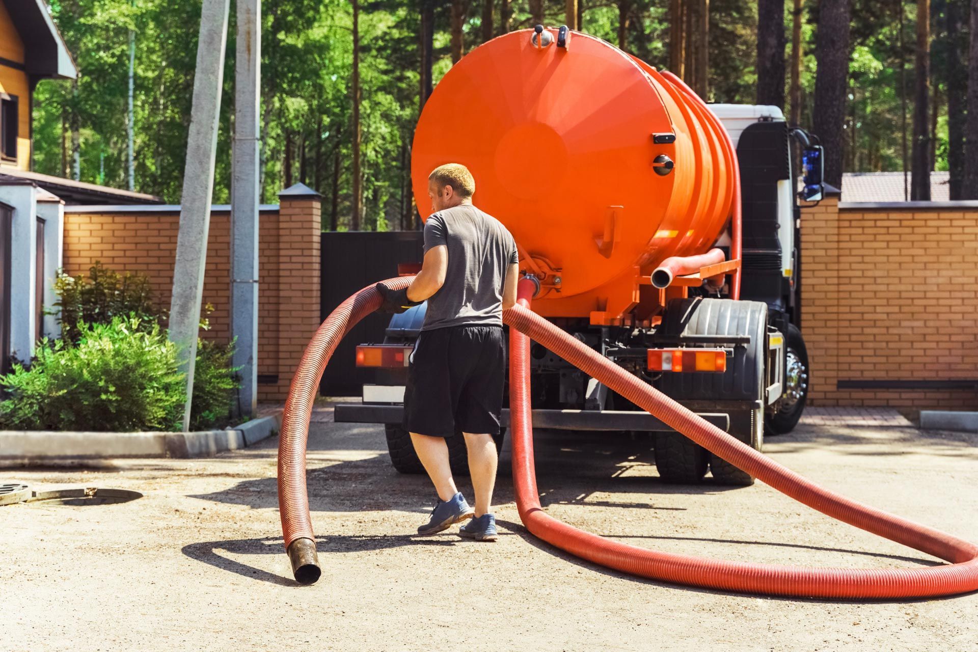 Worker handling a red hose beside an orange septic truck in a residential driveway