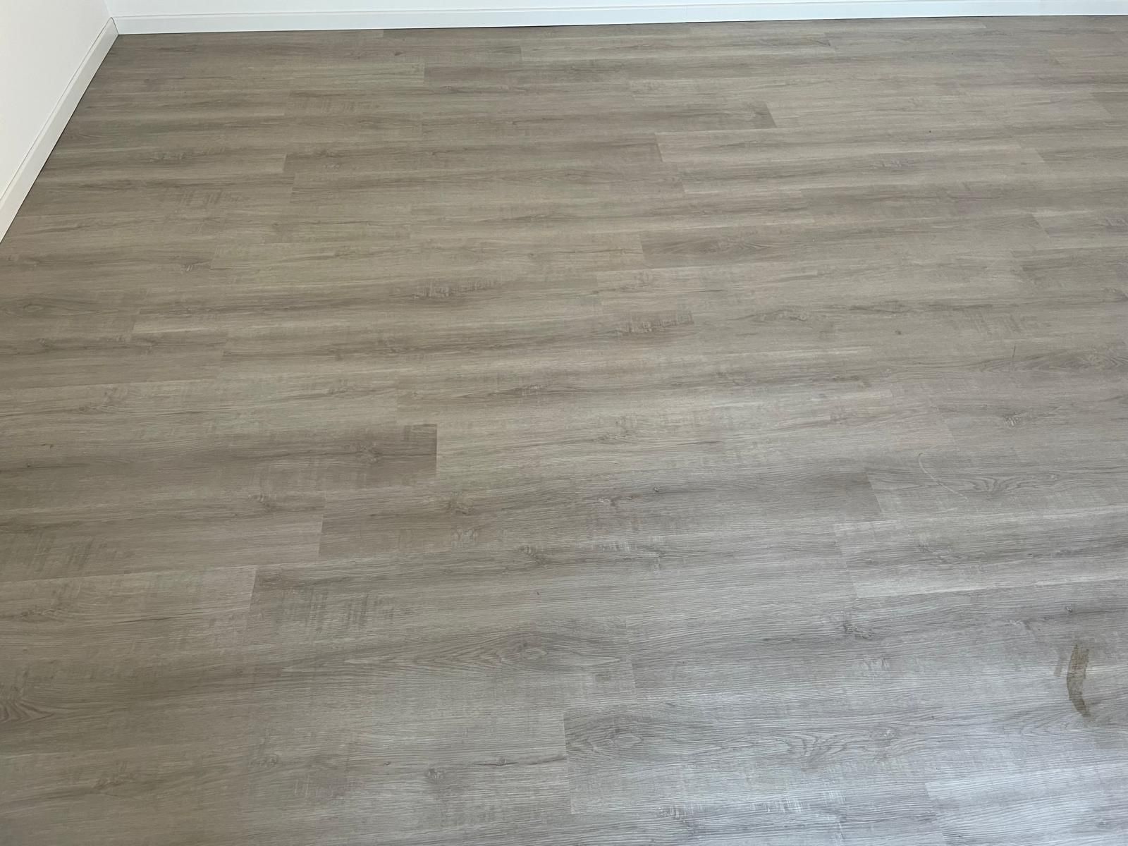 Stanza vuota con pavimento in legno grigio chiaro e battiscopa bianco.