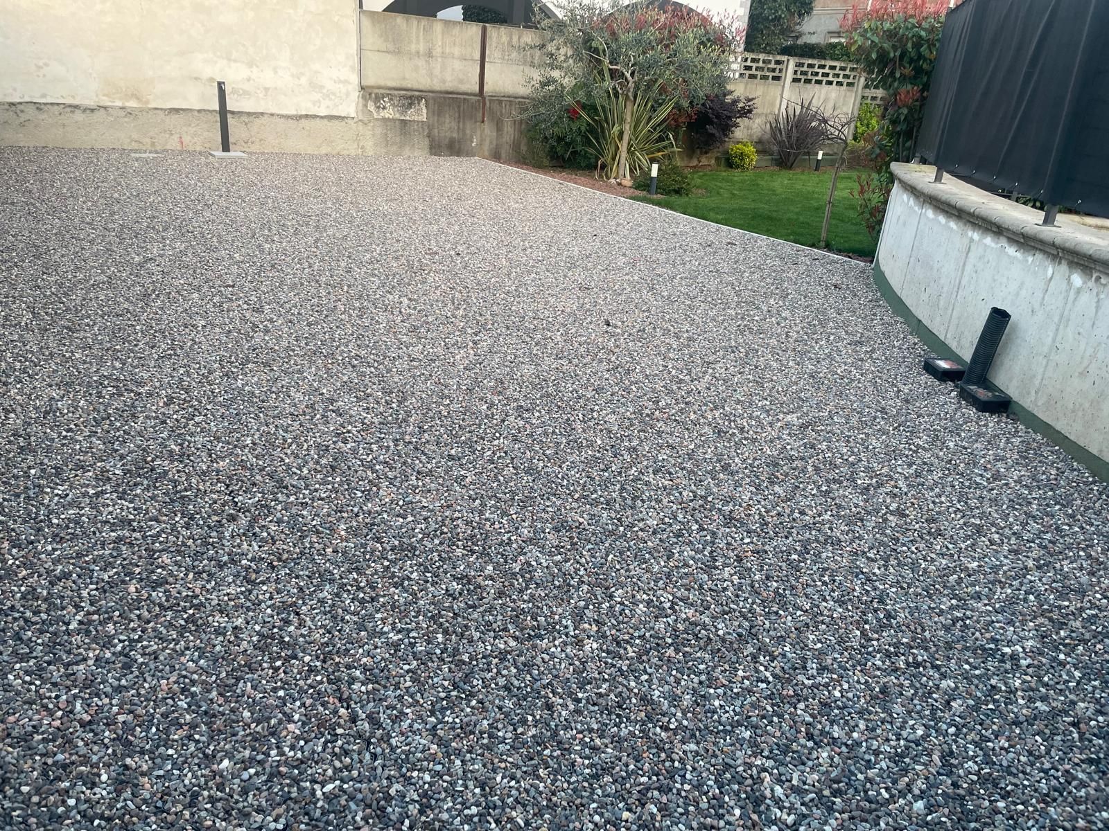 Cortile posteriore ricoperto di ghiaia adiacente a una casa, con una piccola aiuola e una recinzione sullo sfondo.