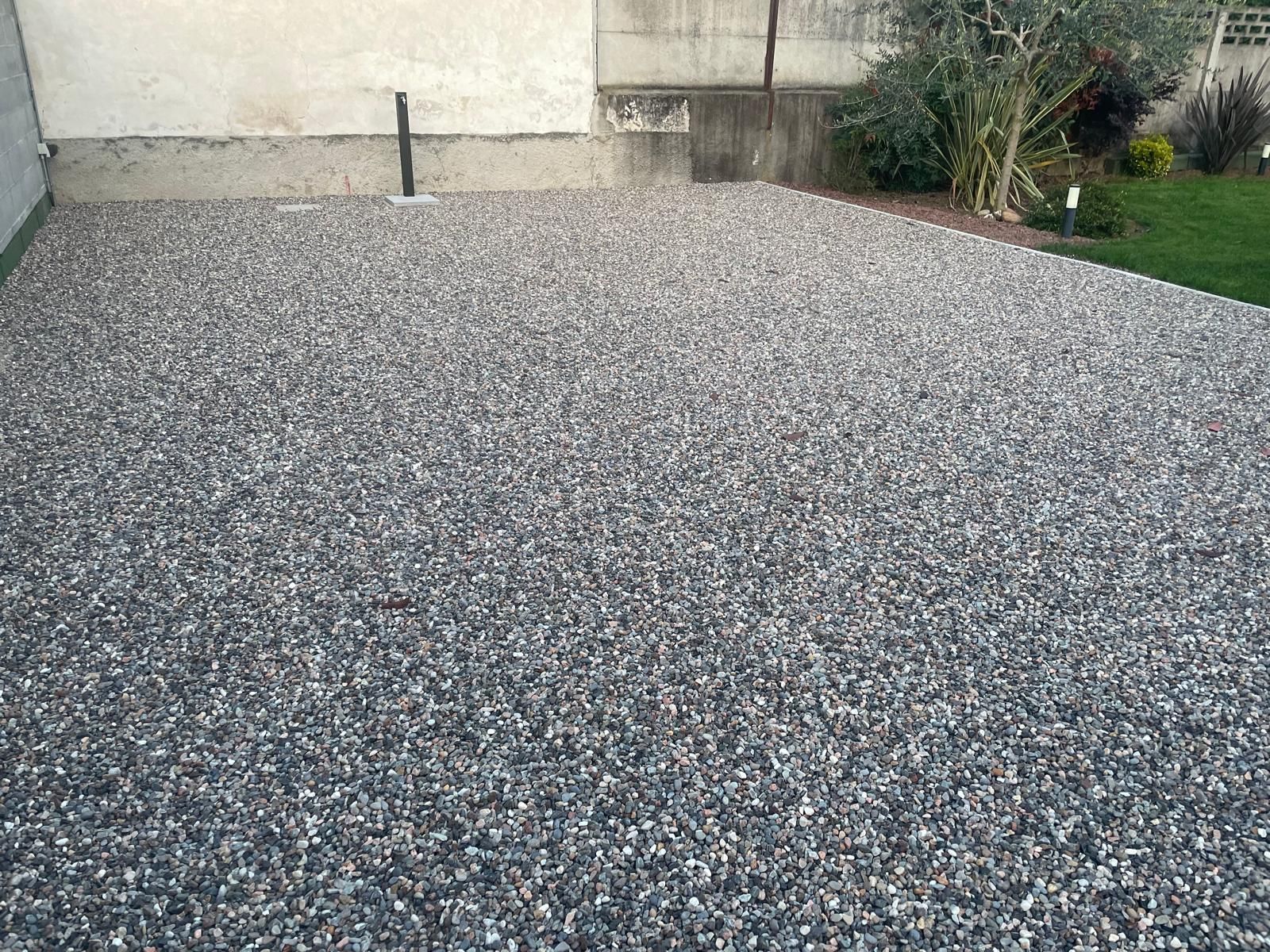 Patio ricoperto di ghiaia accanto a un muro beige e a una piccola aiuola d'erba.