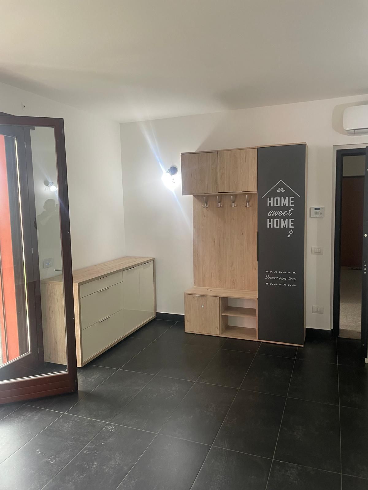 Stanza vuota con pavimento in piastrelle nere, pareti beige, armadio in legno, termosifone e porta a specchio.