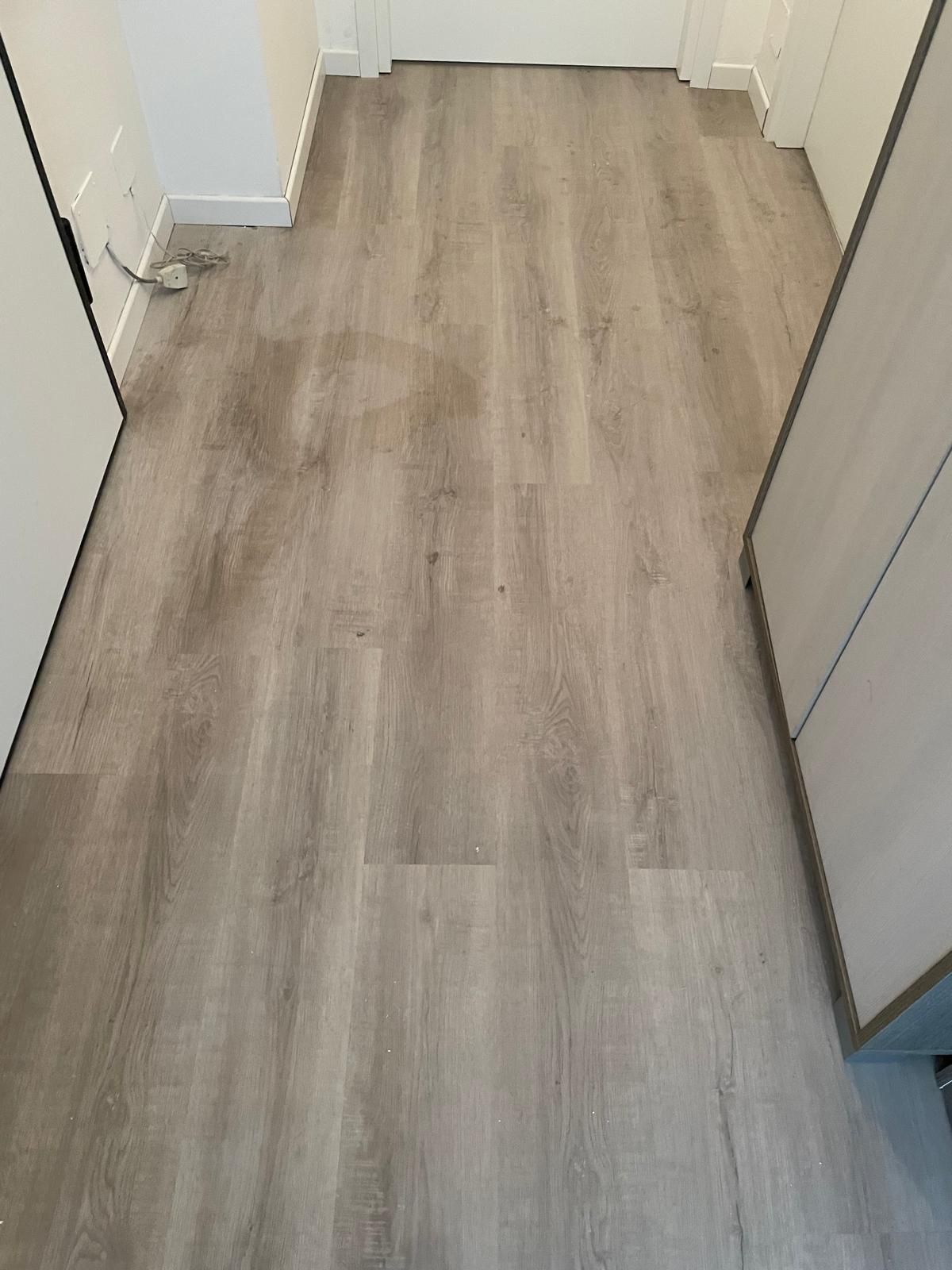 Stretto corridoio con pavimento in legno chiaro e pareti bianche, che conduce a una porta chiusa.