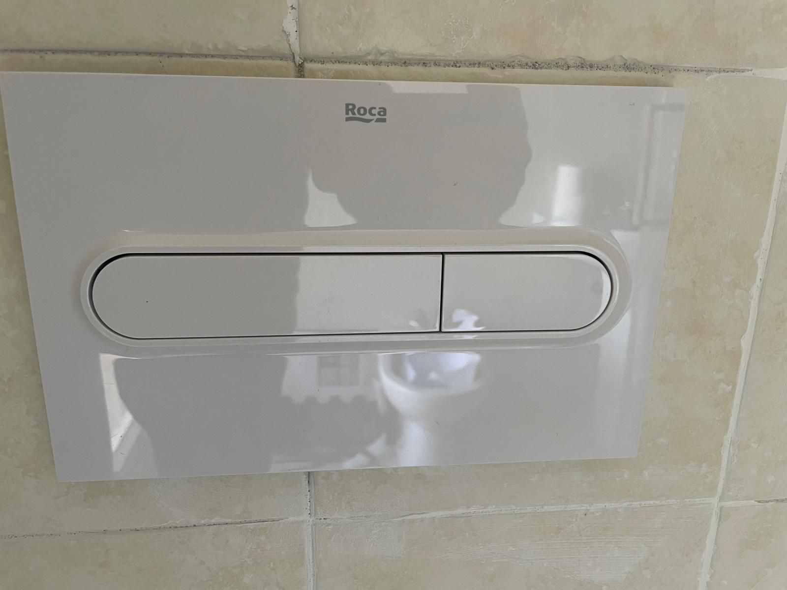 Pannello di controllo a doppio scarico per WC, bianco, a parete su rivestimento in piastrelle beige.