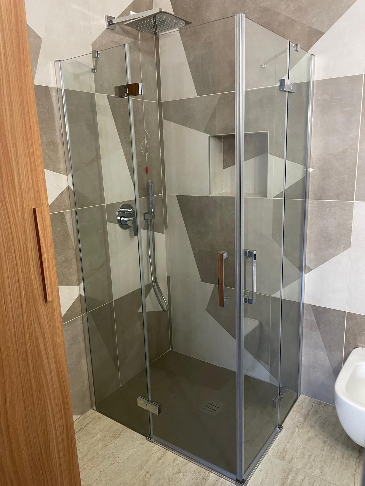 Box doccia angolare in vetro in un bagno piastrellato, con maniglia e rubinetteria cromate.