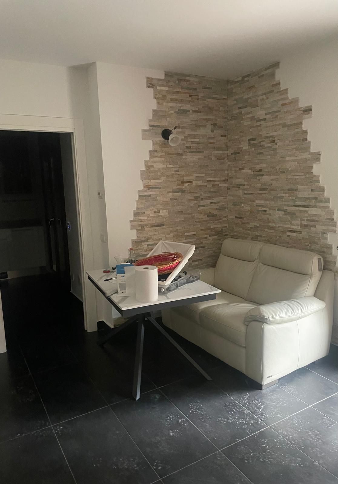 Soggiorno con divano bianco, tavolo pieghevole e parete decorativa in pietra in un angolo.
