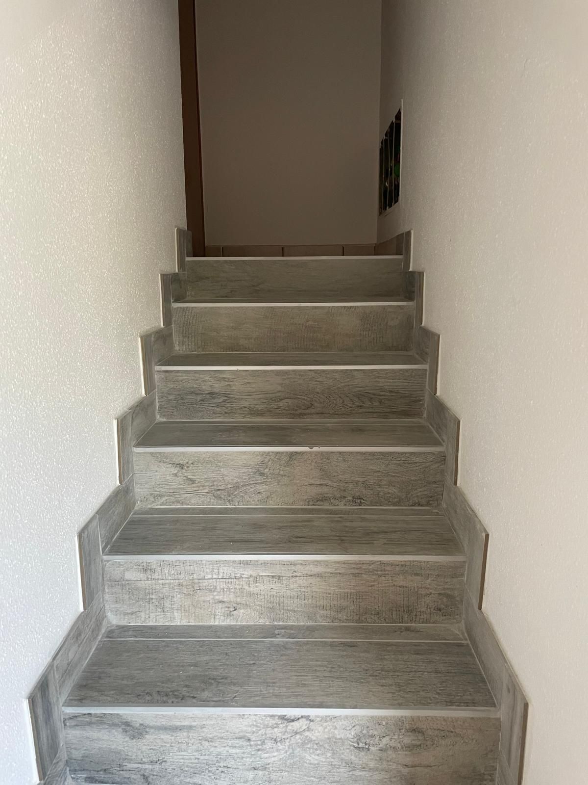 Stretta scala interna con gradini grigi e pareti bianche che conduce verso l'alto a un corridoio.