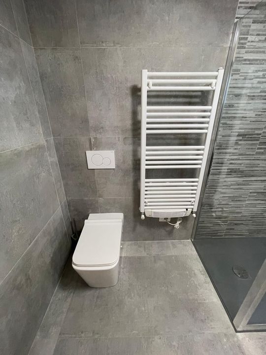 Angolo bagno moderno con WC sospeso e termoarredo bianco su pareti rivestite con piastrelle grigie.
