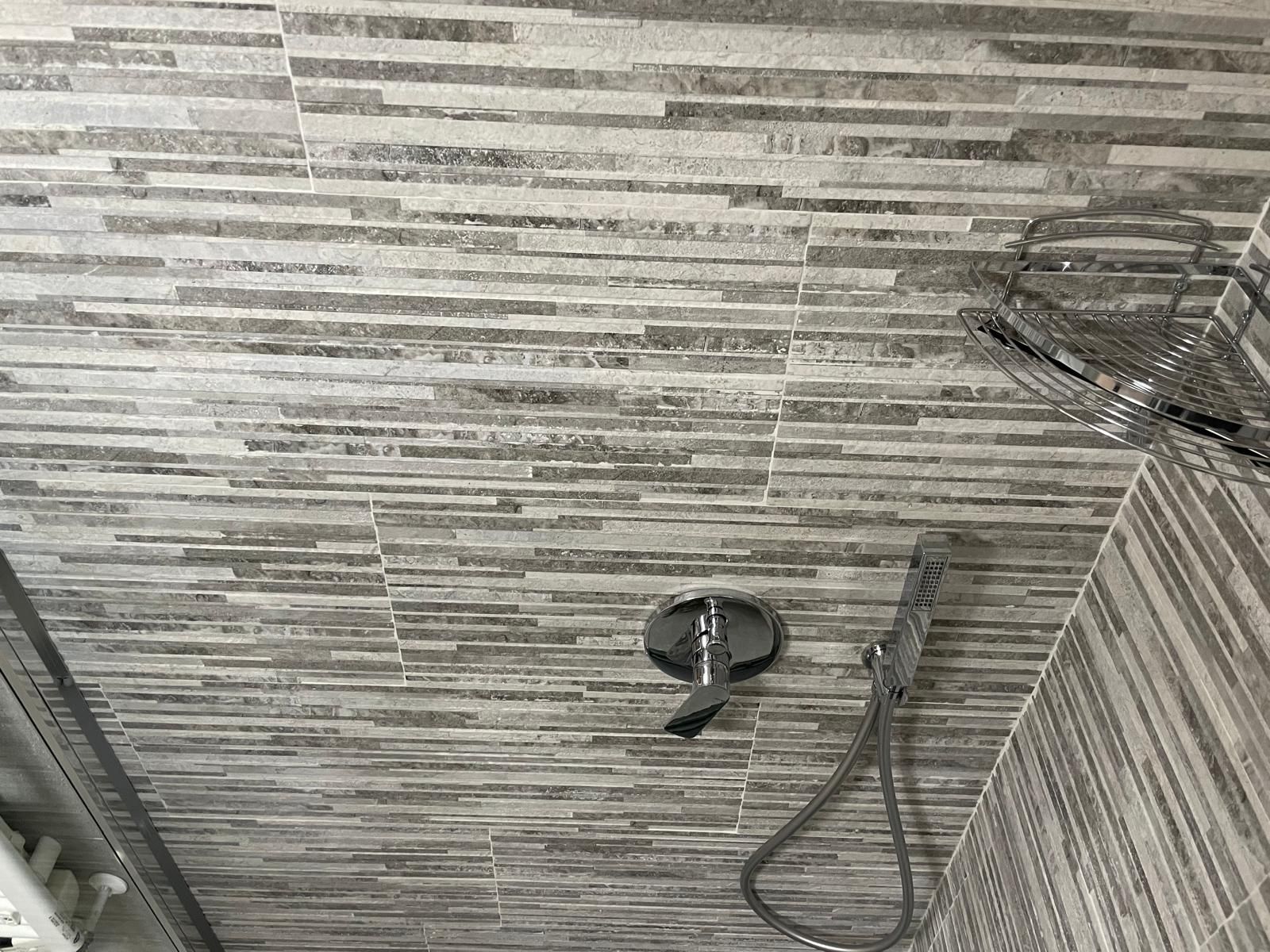 Parete della doccia piastrellata con soffione, flessibile e miscelatore.