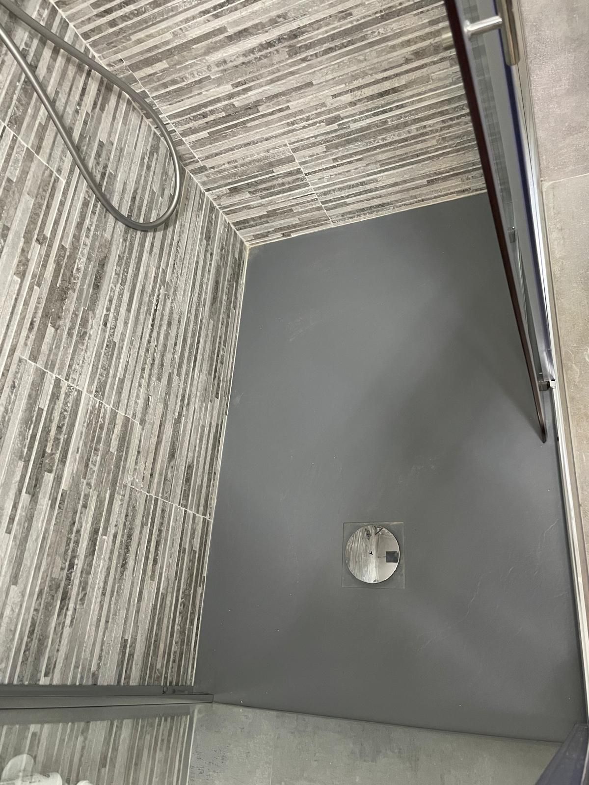 Angolo di parete grigio con soffitto a trama e una piccola lampada circolare vicino al pavimento.