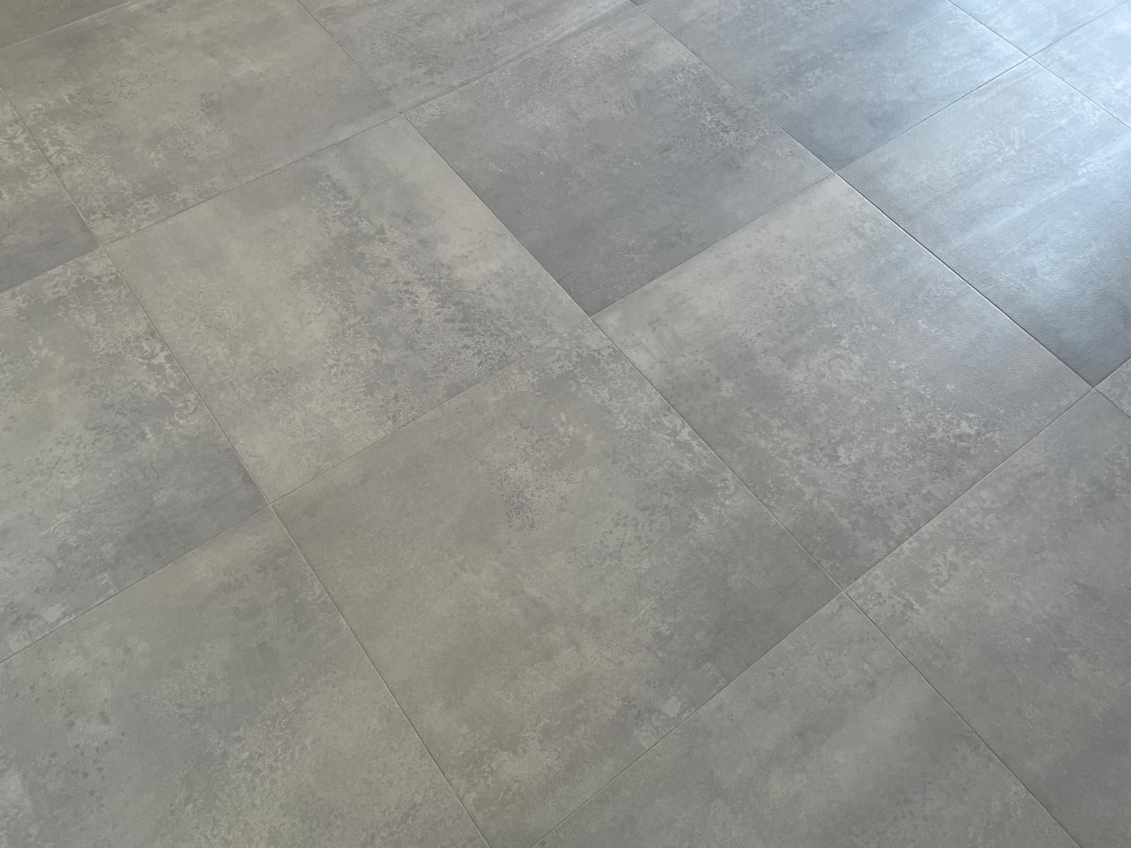 Primo piano di un pavimento in pietra o piastrelle grigie con un delicato motivo geometrico e morbidi riflessi di luce.