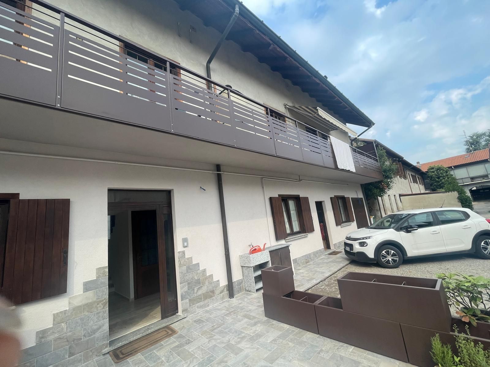 Cortile di una casa bianca a due piani con ringhiere del balcone marroni, porte aperte e un SUV bianco parcheggiato.