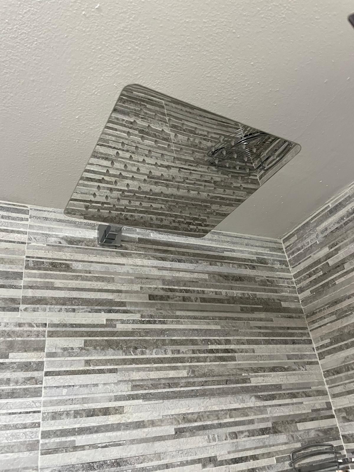 Soffitto del bagno con una macchia scura intorno a una presa d'aria danneggiata o a una zona di perdita sopra le pareti piastrellate.