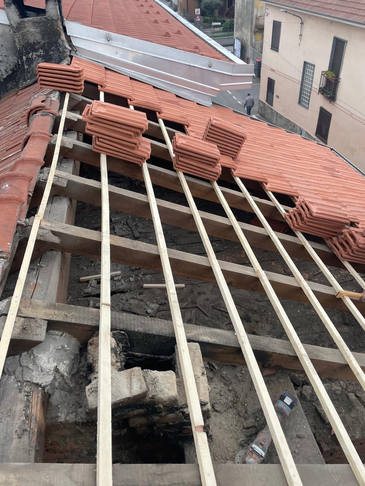 Tetto in costruzione con travi di legno e tegole rosse installate su un tetto danneggiato.