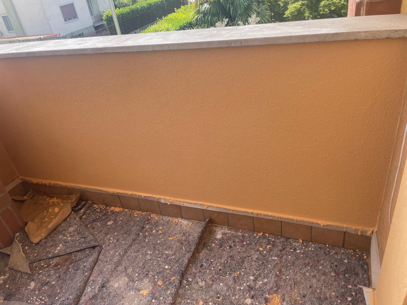 Piccolo balcone piastrellato con pareti beige e vista sul verde oltre la ringhiera