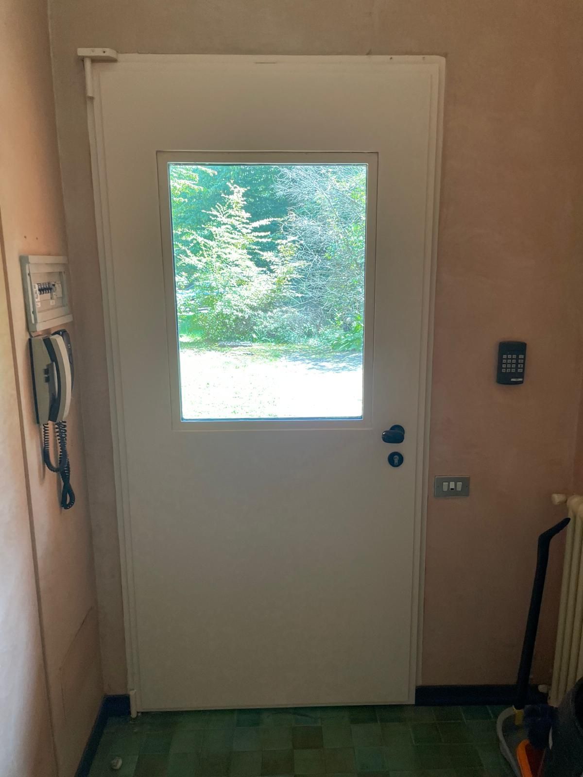 Porta interna con un'ampia finestra che si affaccia su un cortile verde e soleggiato.