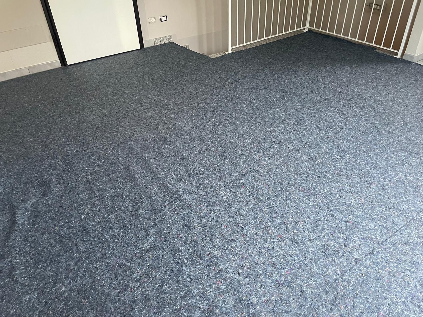 Stanza vuota con moquette, pavimento grigio maculato e pareti color beige, vicino a una ringhiera e a una porta.