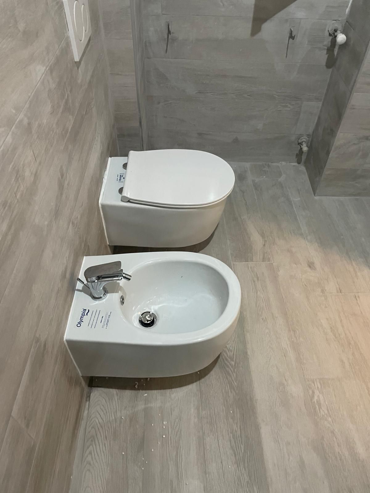 Piccolo bagno con WC e bidet bianchi su pavimento piastrellato beige.