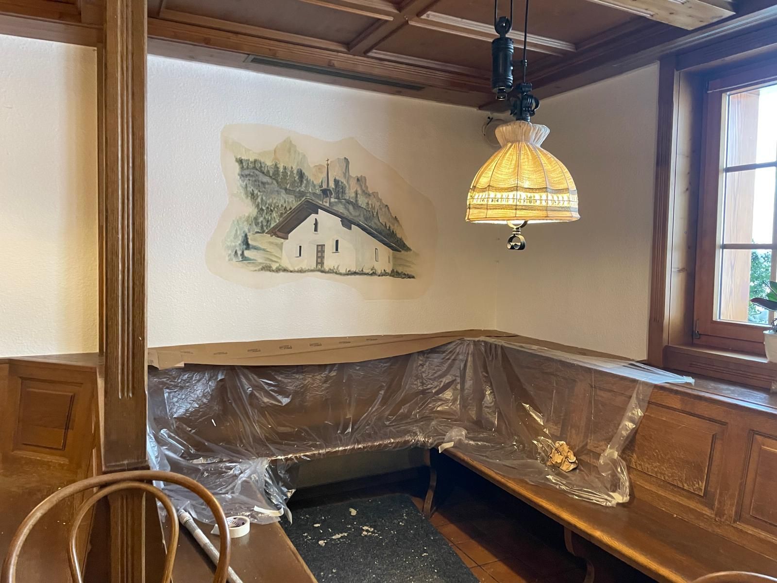 Cabina da ristorante con pannelli in legno, panca rivestita in plastica, lampada a sospensione e murale sulla parete.