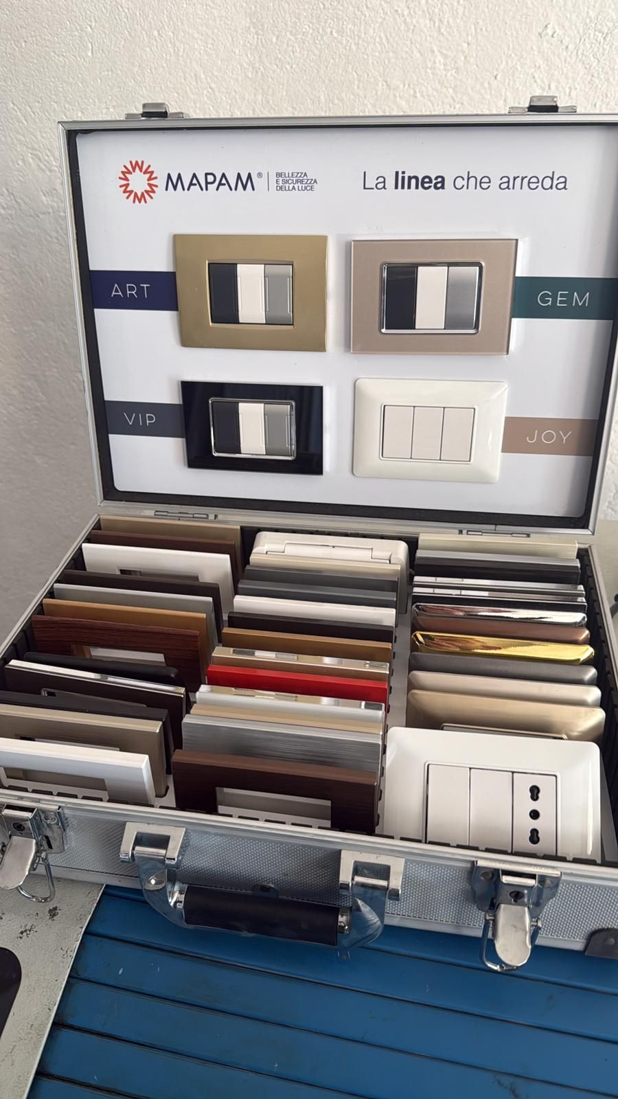Esposizione di interruttori elettrici e campioni in uno showroom, con pannello prodotti a parete e vassoio di materiali.