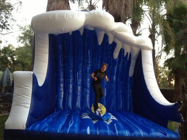 Person surfing an inflatable wave. The wave is blue and white, with the person balancing on a surfboard.