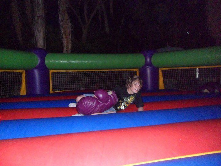 Child wearing purple boxing gloves crawling in an inflatable boxing ring with a dark background.
