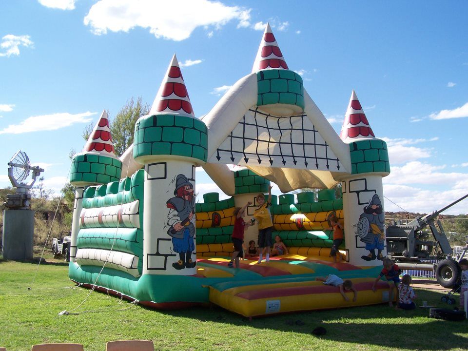Bouncy castle shaped like a green and white castle with red accents. Children play inside on a sunny day.