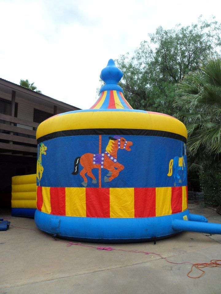 Blue, yellow, and red carousel-themed inflatable bounce house set up on a concrete driveway.