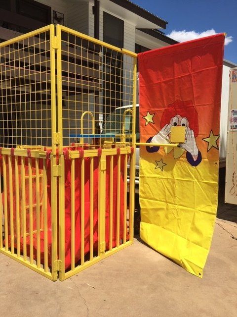 A yellow and red dunk tank with a clown target, ready for use outdoors on a sunny day.