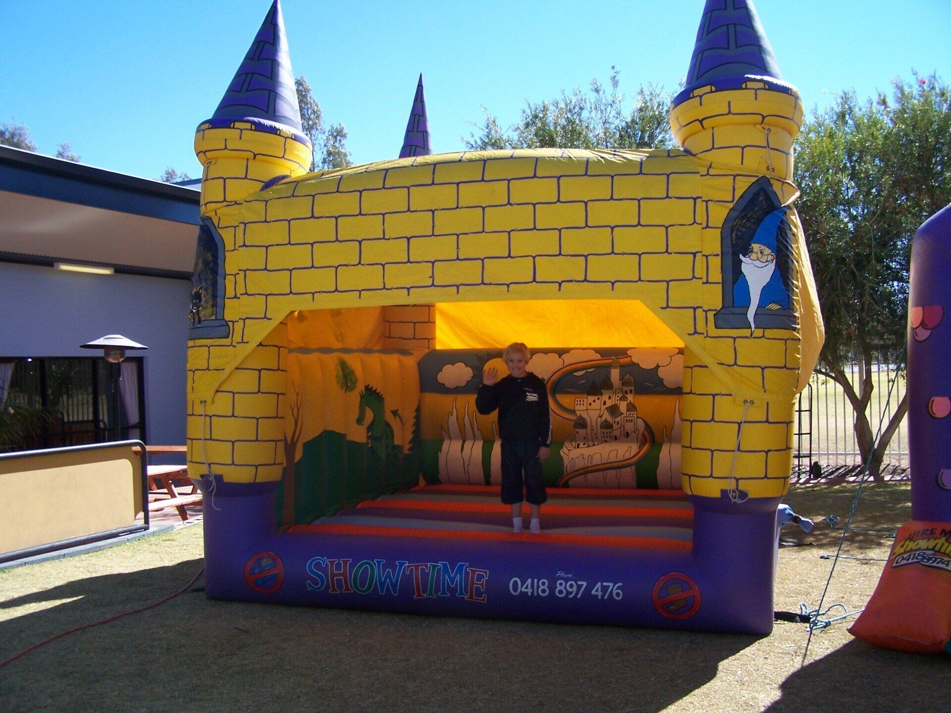 Child standing inside a yellow and purple inflatable castle bounce house on a sunny day.