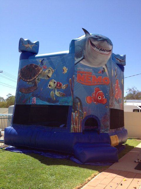 A blue Finding Nemo-themed bouncy castle with shark and turtle designs on a grassy lawn.