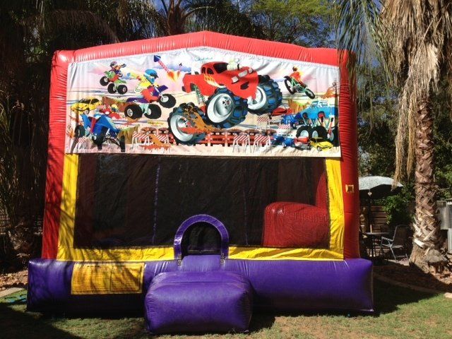 Red, yellow, and purple inflatable bounce house with racing graphics in a grassy outdoor setting.