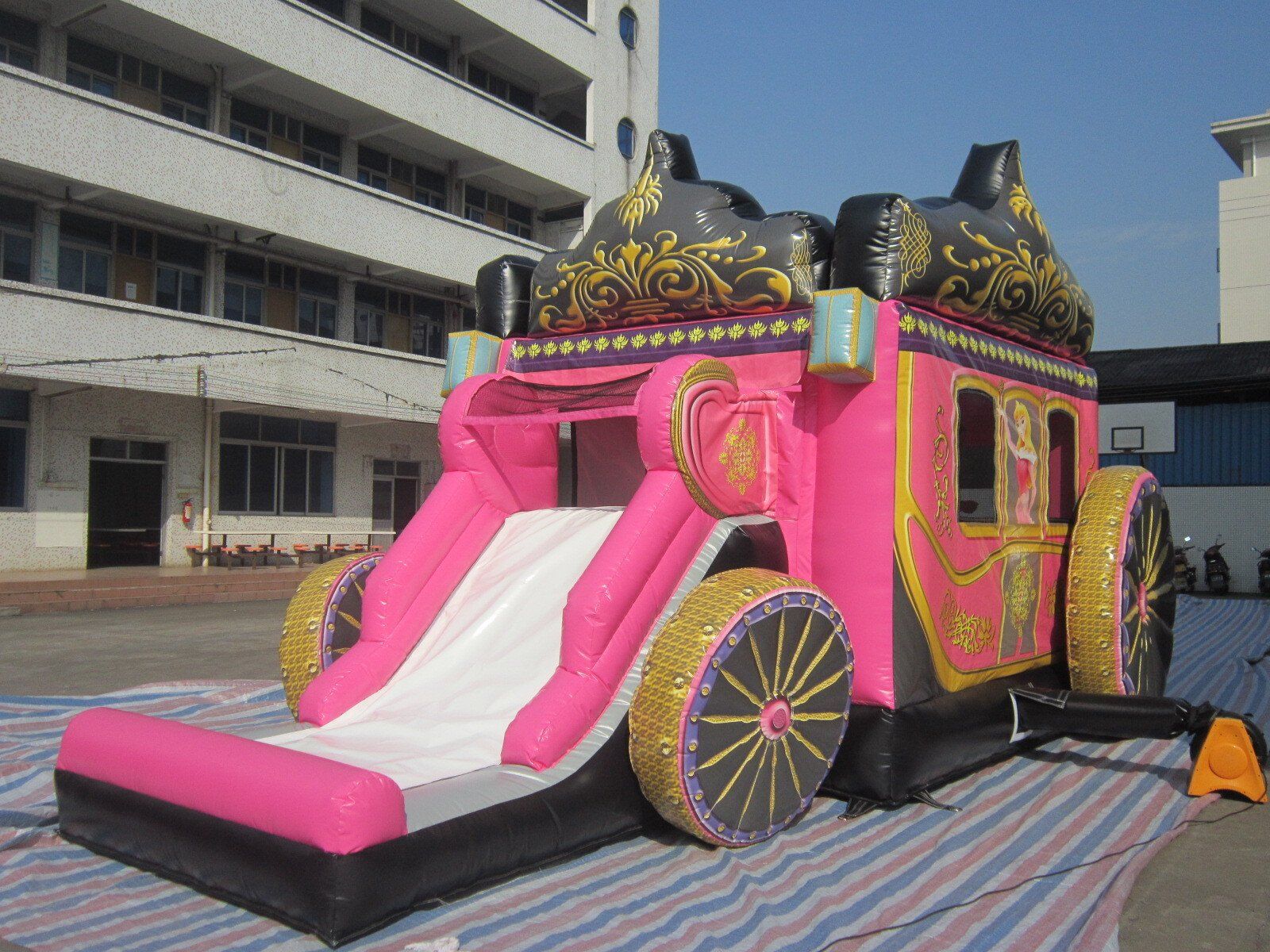 Pink inflatable princess carriage with a slide, set outdoors.