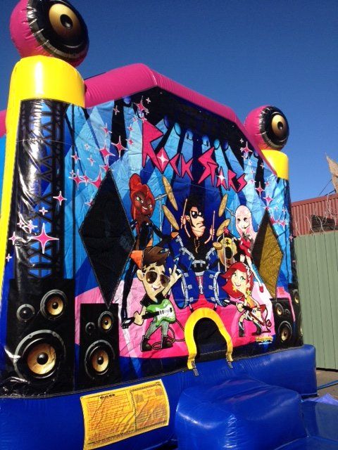 A colorful inflatable bounce house featuring a rock band theme with cartoon characters, speakers, and stars.