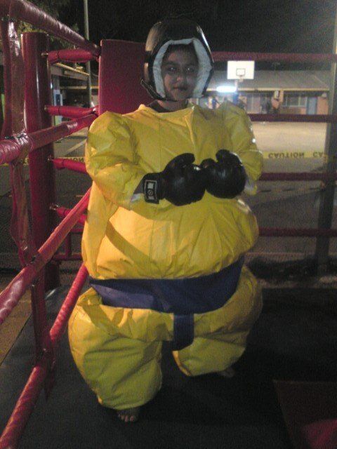 Person in a yellow sumo wrestling suit with headgear and black gloves stands in a boxing ring.