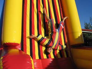 A person in a colorful jumpsuit is upside down on a vertical inflatable wall with yellow, red, and black stripes.