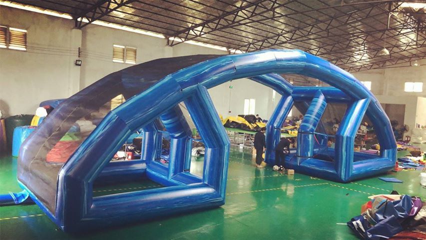 An inflatable blue tunnel structure inside a warehouse, with a dark, patterned roof.